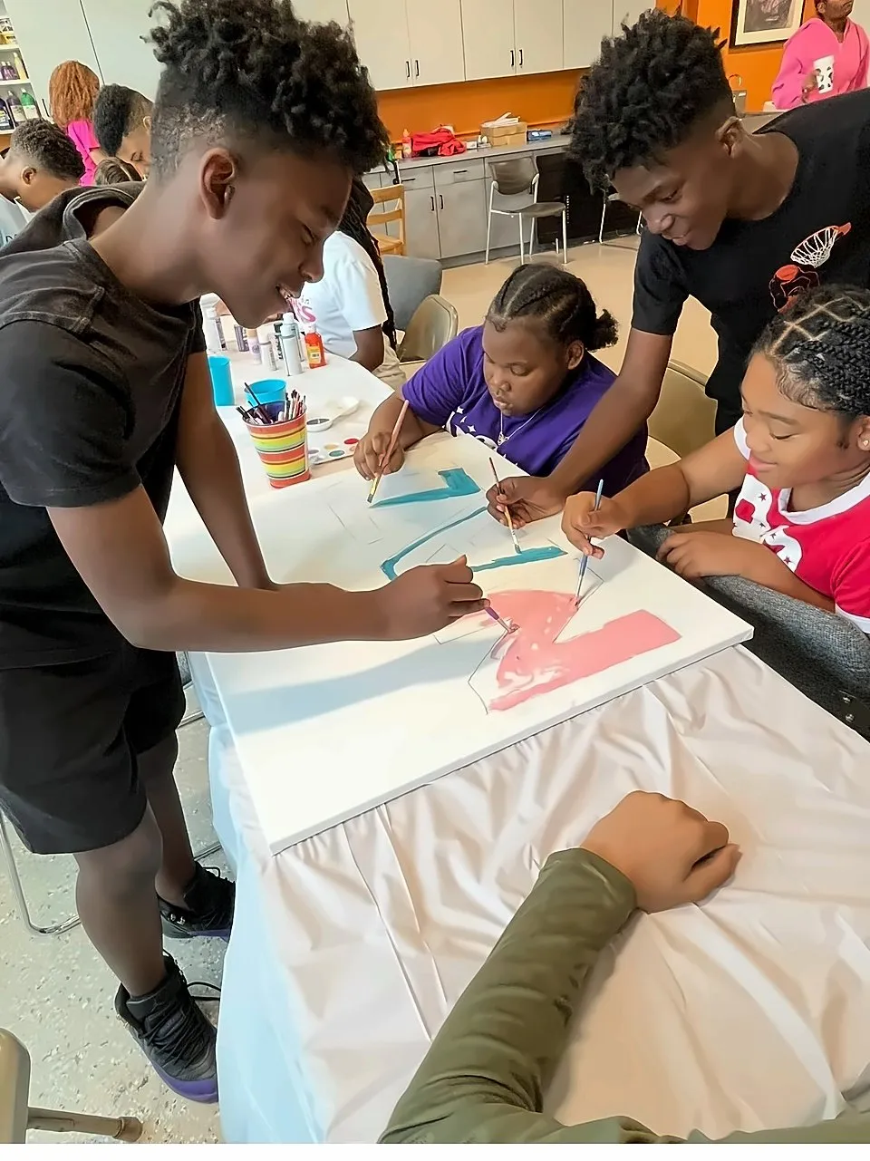Teen mentors helping younger students paint a large canvas